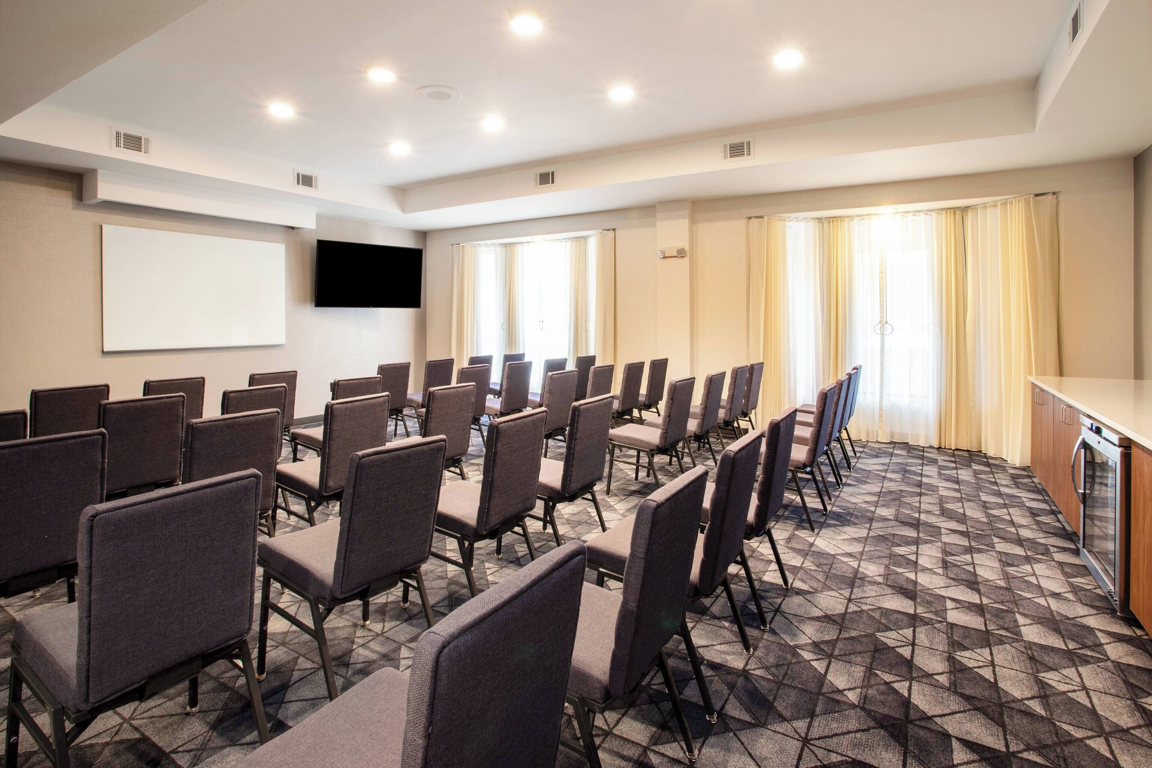 A conference room with rows of chairs, a projector screen, and a kitchen area.