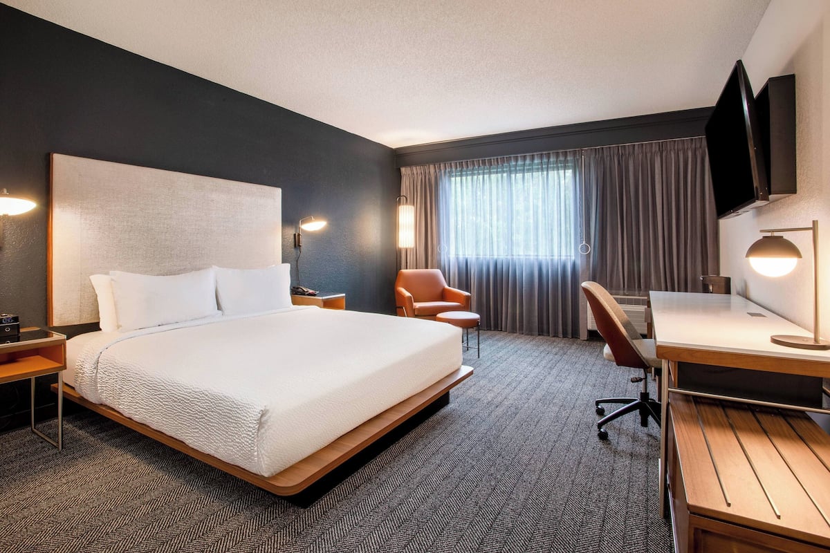 A hotel room with a large bed, a desk, a chair, a TV, and a window with curtains.
