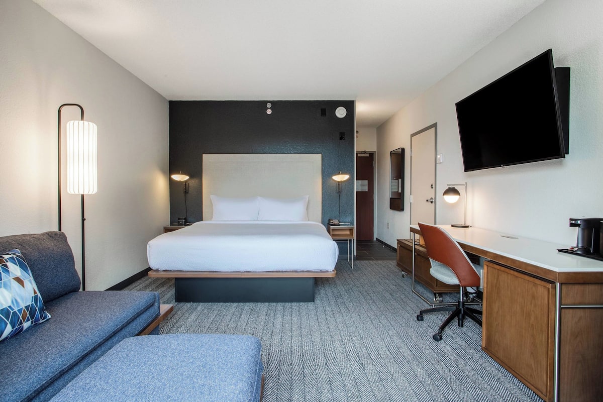 A hotel room with a large bed, a desk, a chair, a sofa, and a flat-screen TV.