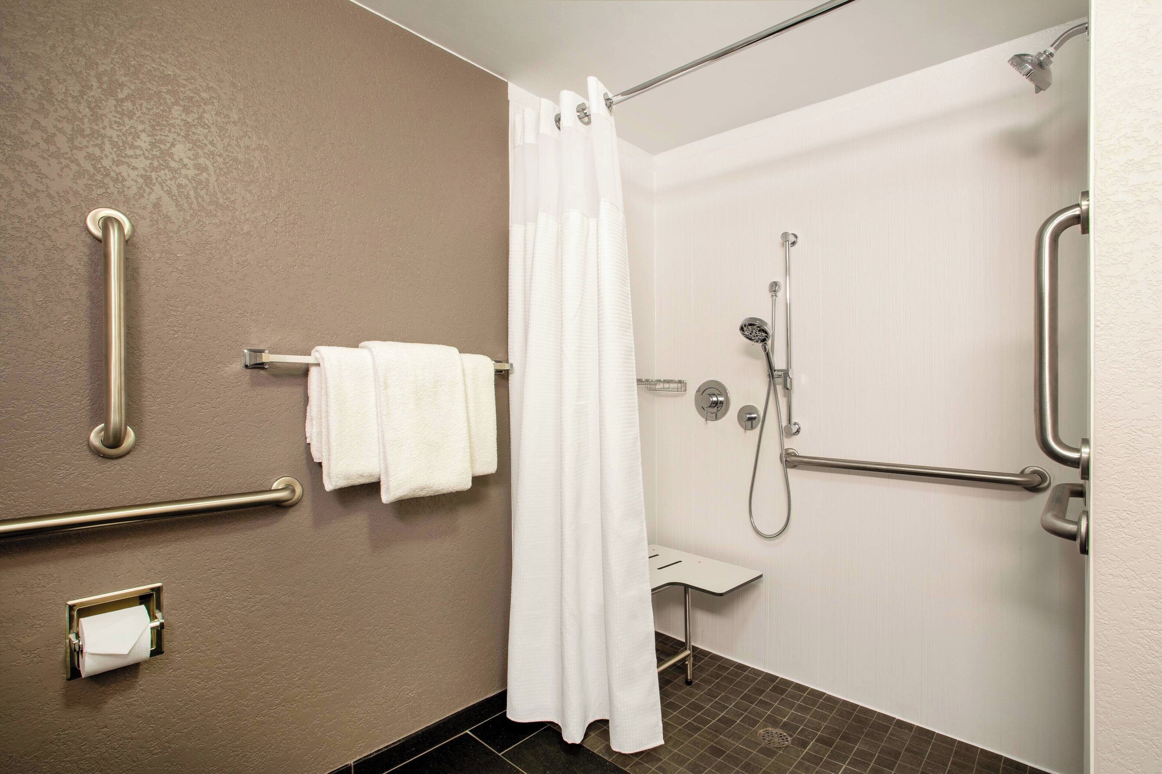 Une salle de bain équipée d’une douche, de barres d’appui, d’un porte-serviettes et de toilettes.