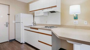 A compact kitchen with white cabinets, a built-in stove, and a wall-mounted light fixture. - Extended Stay America Select Suites Orlando Southpark (Orlando)