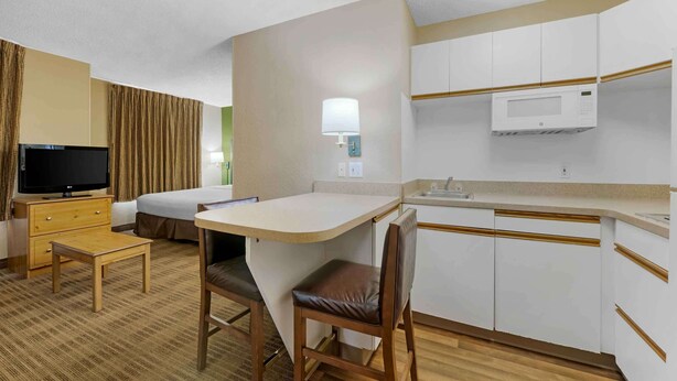 A hotel room with a kitchenette, a TV, a bed, and a desk with a chair. - Extended Stay America Select Suites Orlando Southpark (Orlando)