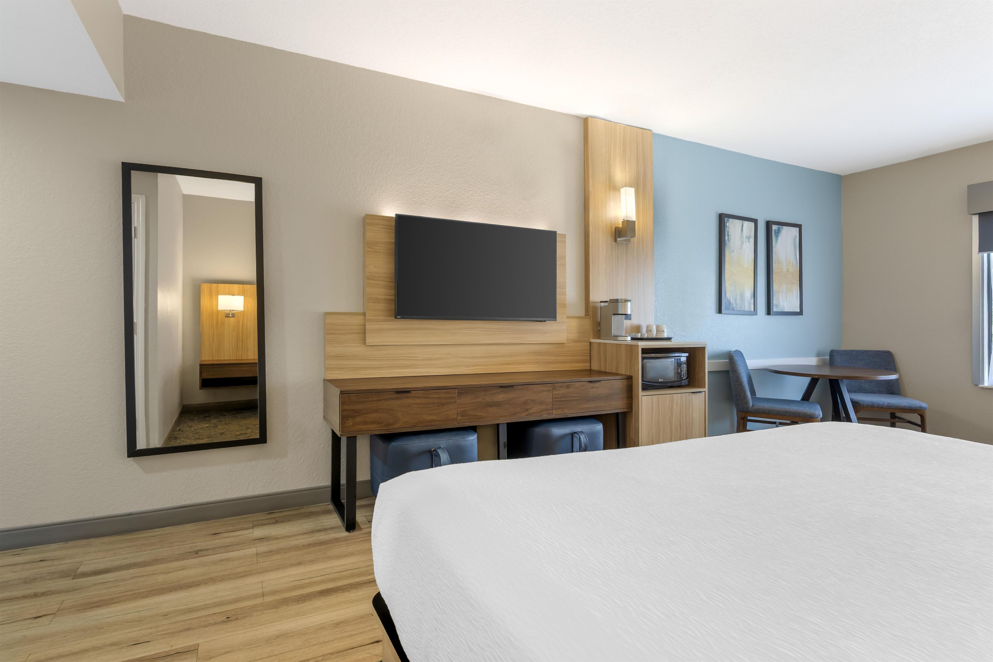 Una camera d'albergo con un letto, una scrivania, una sedia, un televisore e un tavolino con forno a microonde.