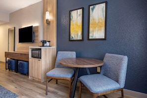 Habitació d'hotel moderna amb escriptori de fusta, televisió de pantalla plana, microones i dues butaques tapissades.
