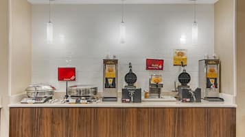 A breakfast bar with waffle batter dispensers, a sign for Energize Proteins, and a sign for building.