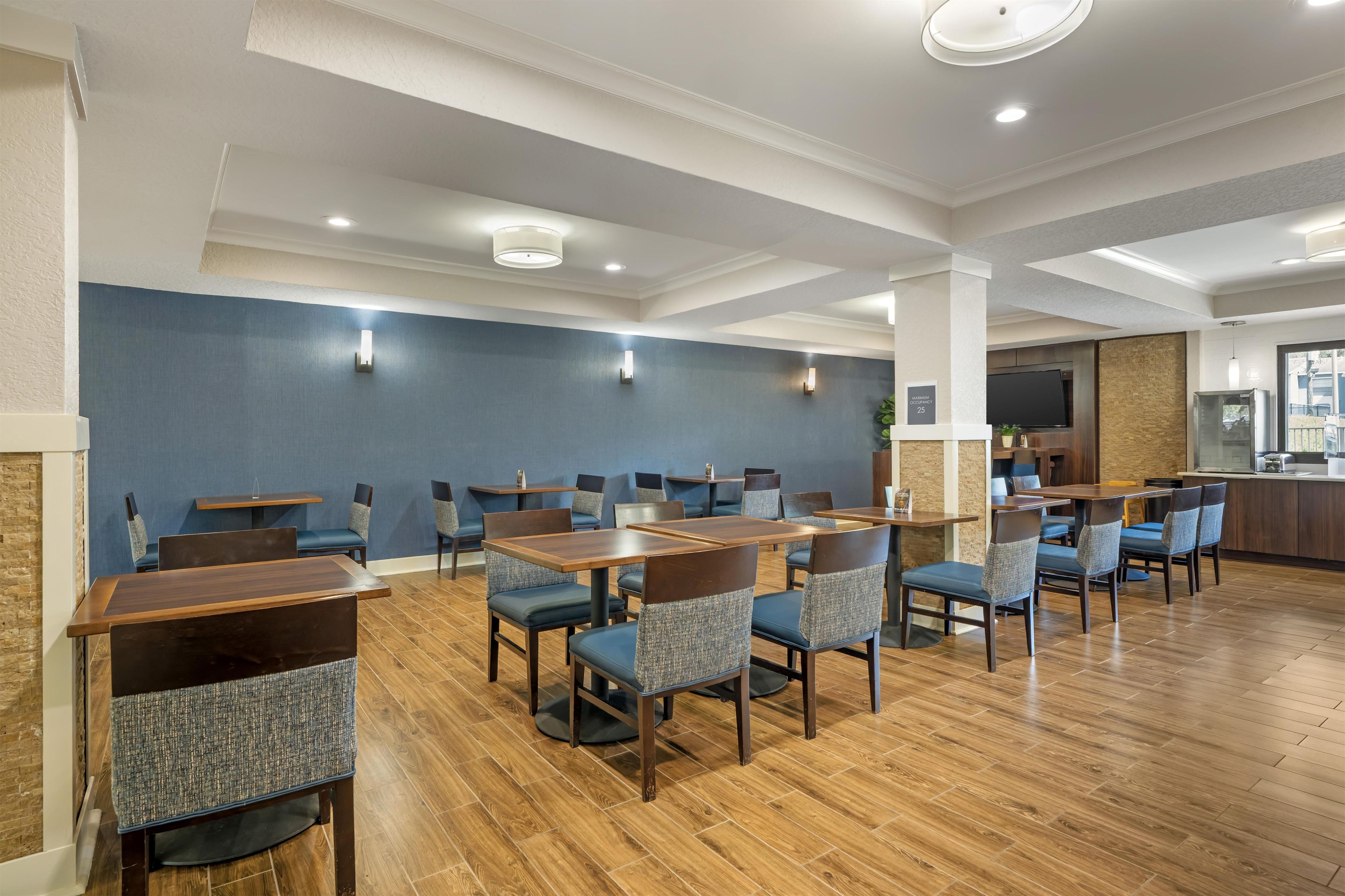 A hotel lobby with a modern design, featuring a mix of seating arrangements, a kitchen area, and a large screen TV.