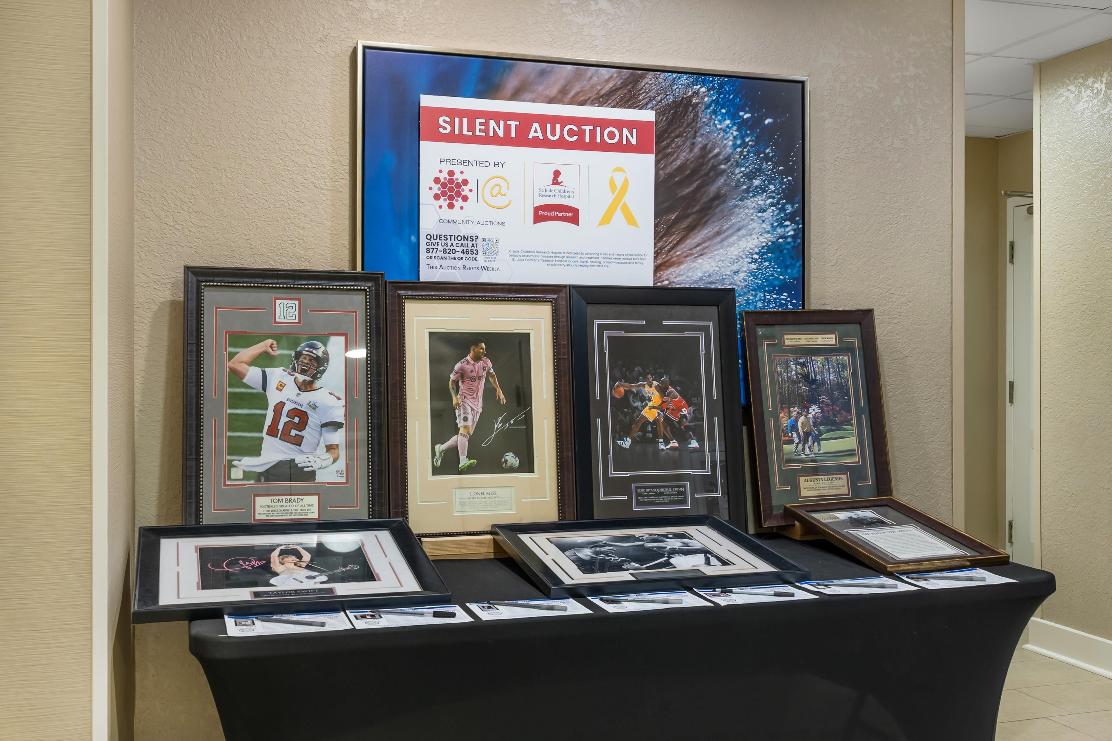 Een stille veilingtafel met ingekaderde sportmemorabilia en een poster die het evenement promoot.