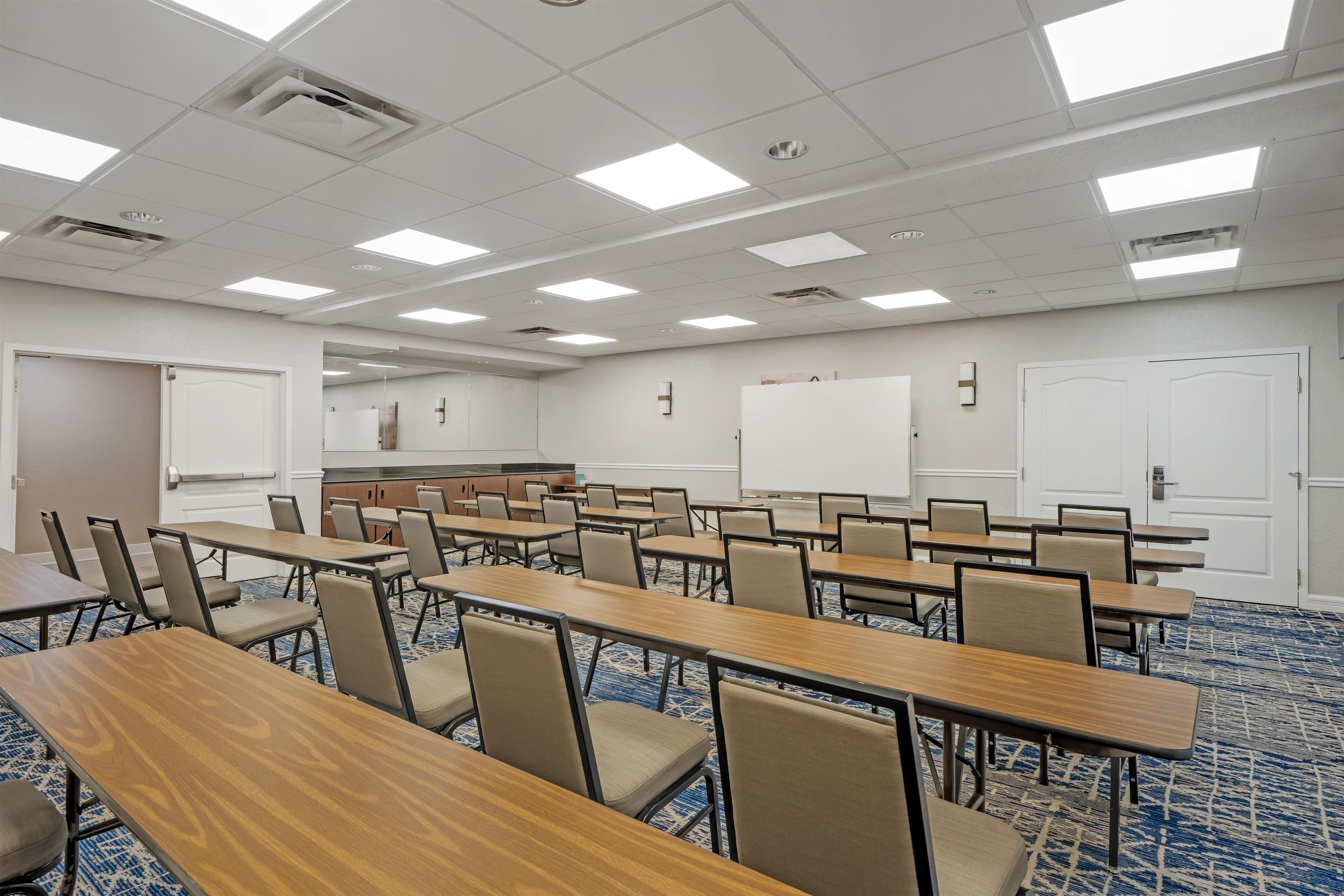A conference room with multiple tables and chairs, a whiteboard, and a projector screen.