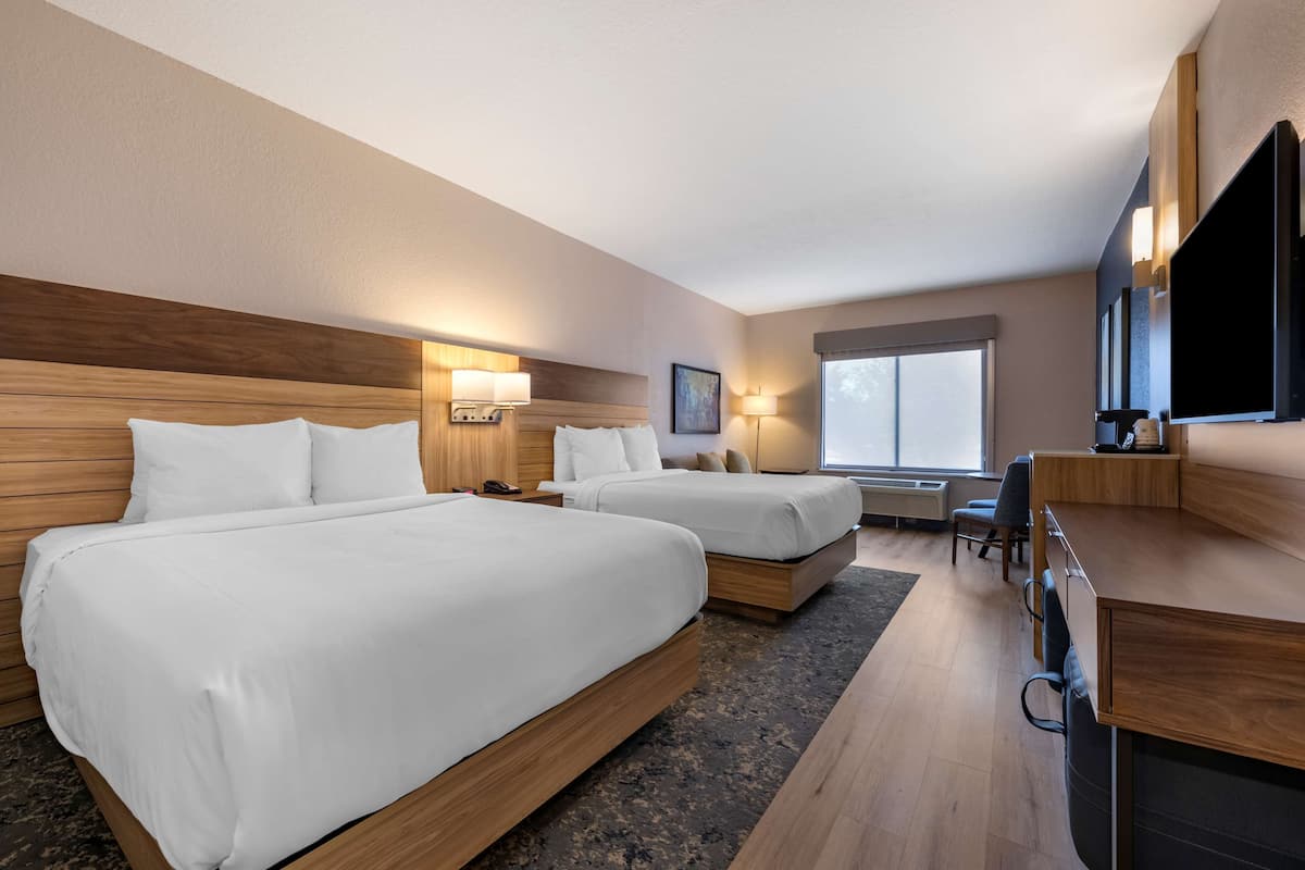 A hotel room with two beds, a desk, and a large window.