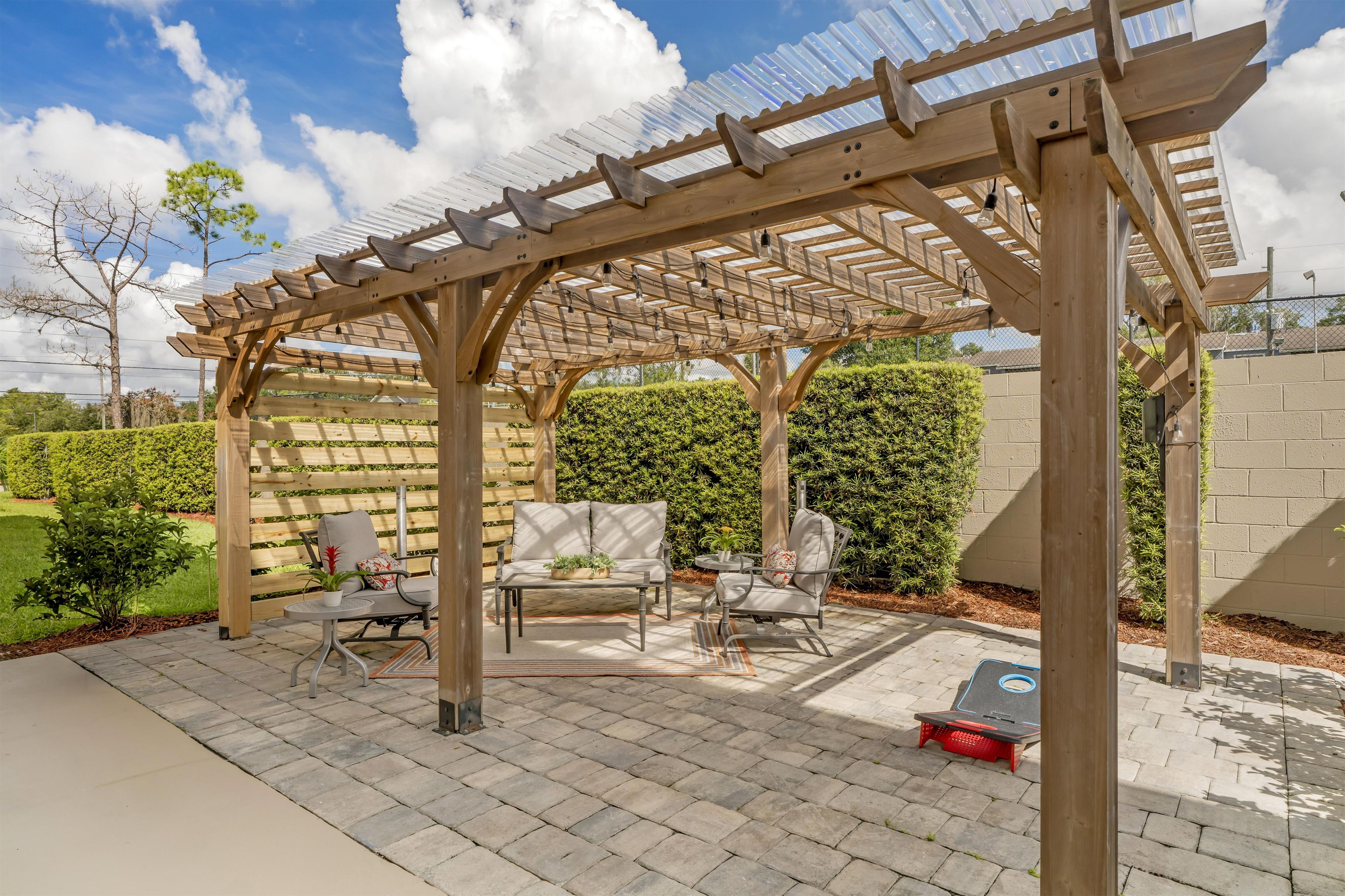 A wooden pergola with a seating area underneath, including a table and chairs.