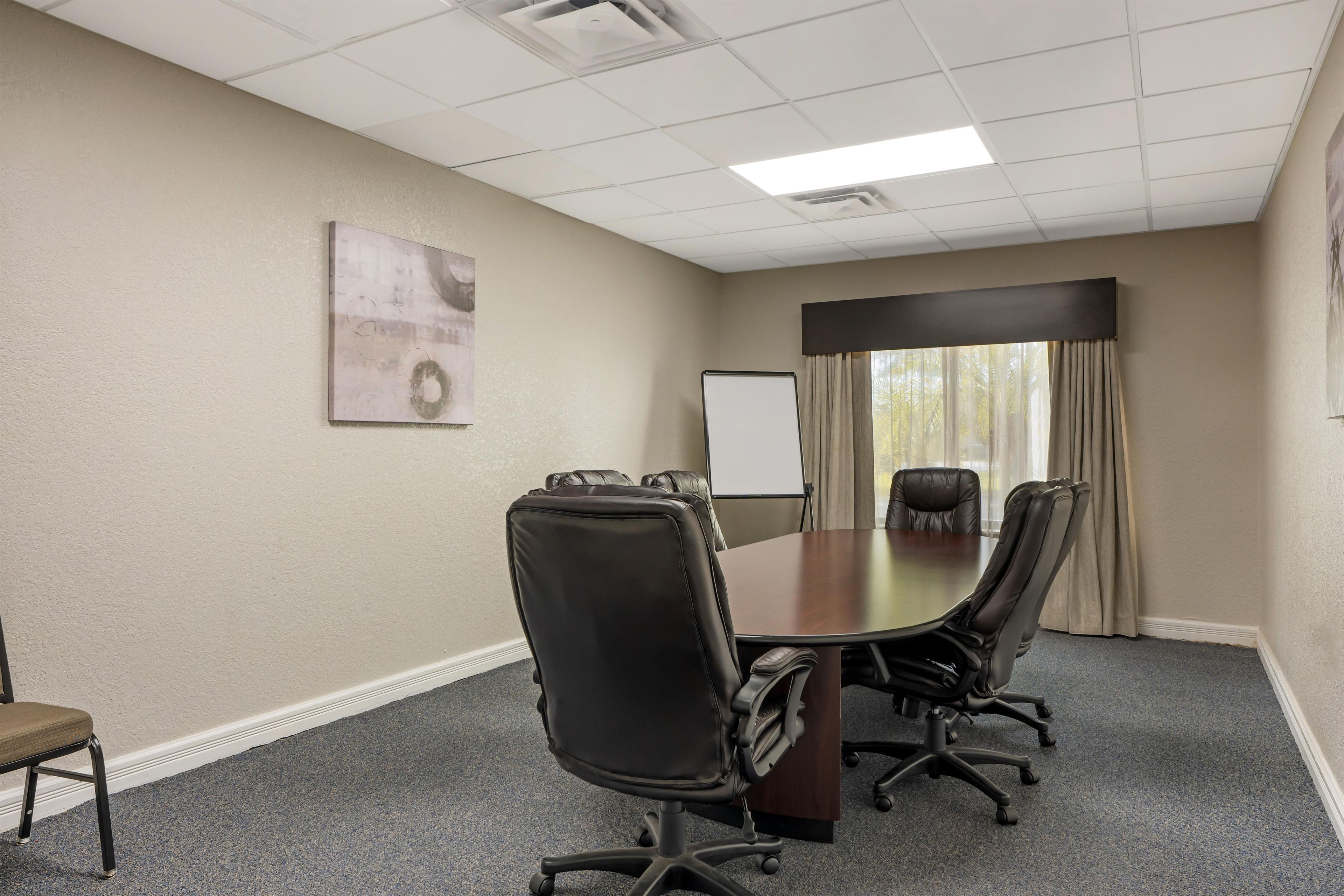 A conference room with a large table, four chairs, a whiteboard, and a painting on the wall.
