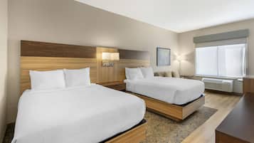 A hotel room with two beds, a nightstand, a lamp, a window with blinds, and a radiator.