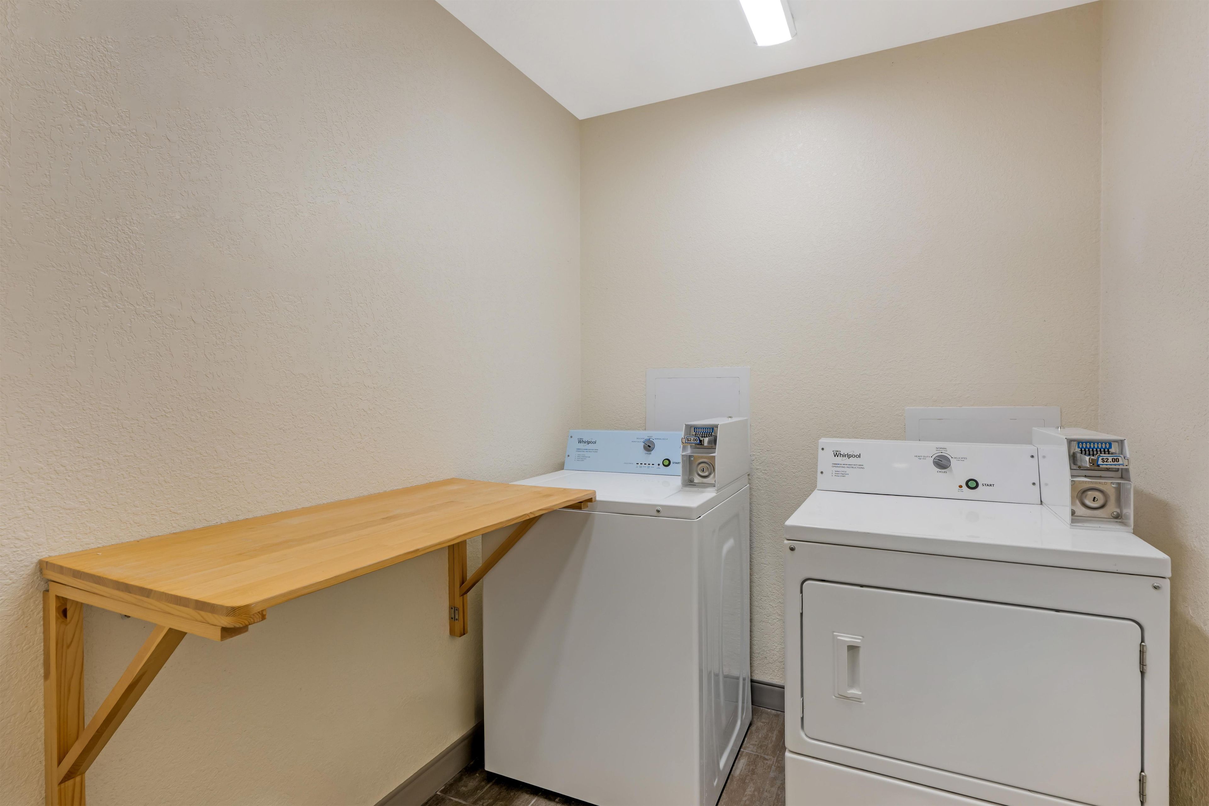 A laundry room with two stacked washers and dryers, a wooden bench, and a skylight.