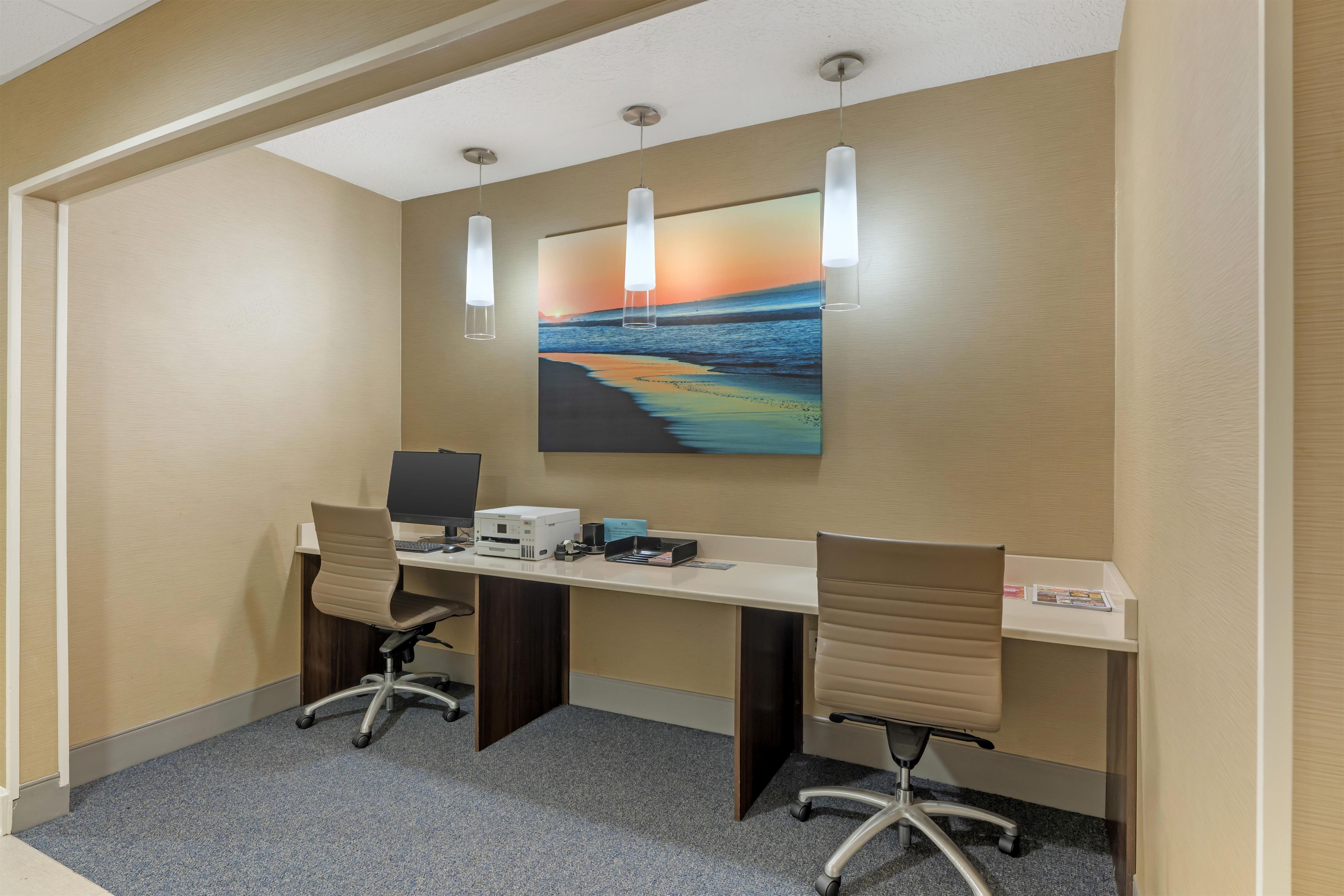 A conference room with a desk, two chairs, a computer, and a painting of a sunset over the ocean.