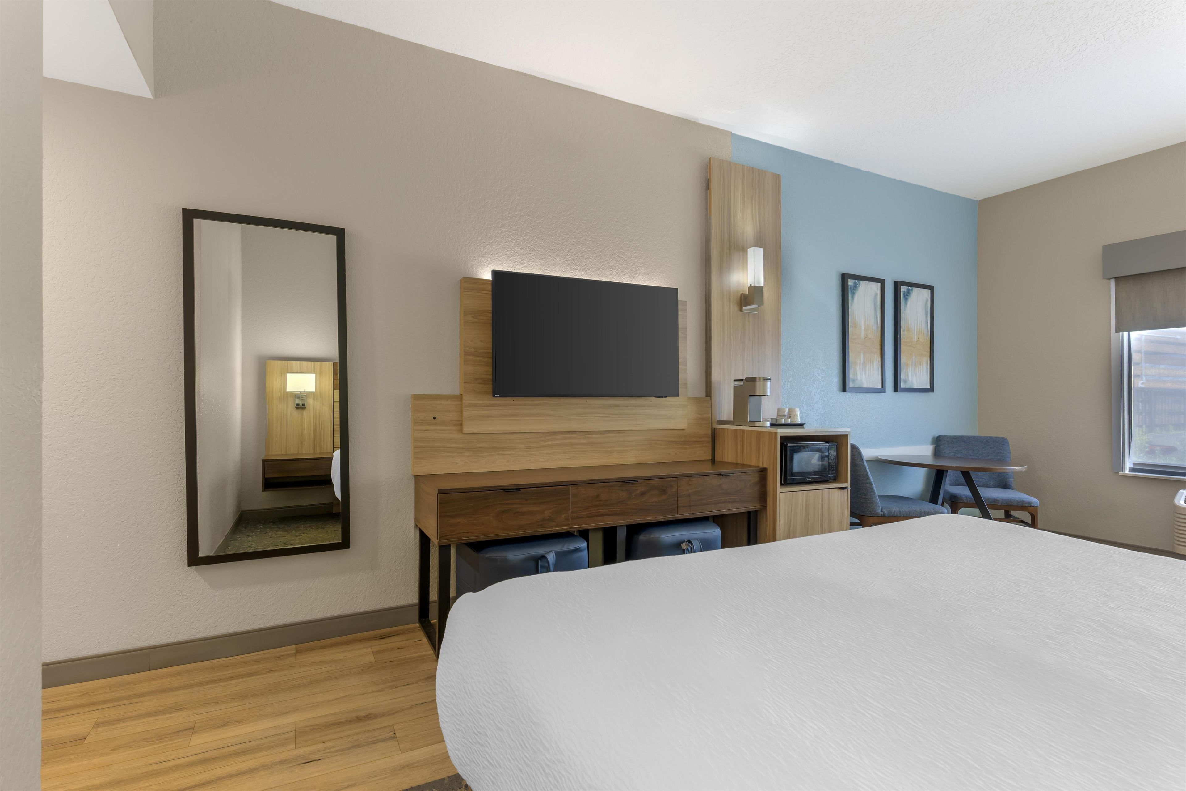 Una camera d'albergo con un letto grande, una scrivania con televisione a schermo piatto, una sedia, un tavolino e un forno a microonde.