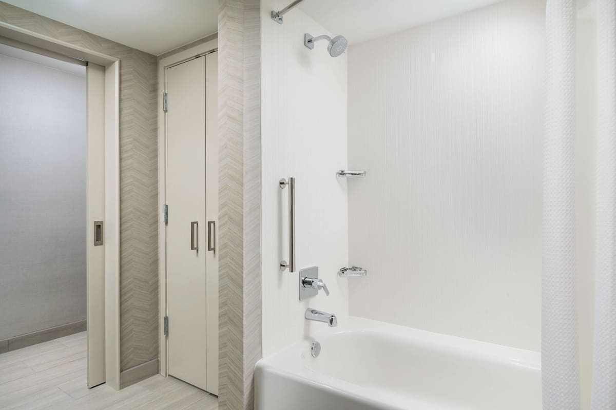 Ein modernes Badezimmer mit freistehender Badewanne, Dusche und einer Tür mit Wandverkleidung in Fischgrätmuster.