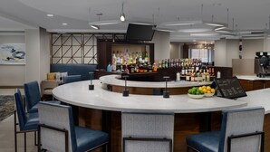 Un área de bar moderna con una barra curva, taburetes y una variedad de botellas de licor.
