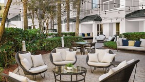 Un patio al aire libre con mobiliario de mimbre, una mesa de vidrio y vistas a un edificio en el fondo.
