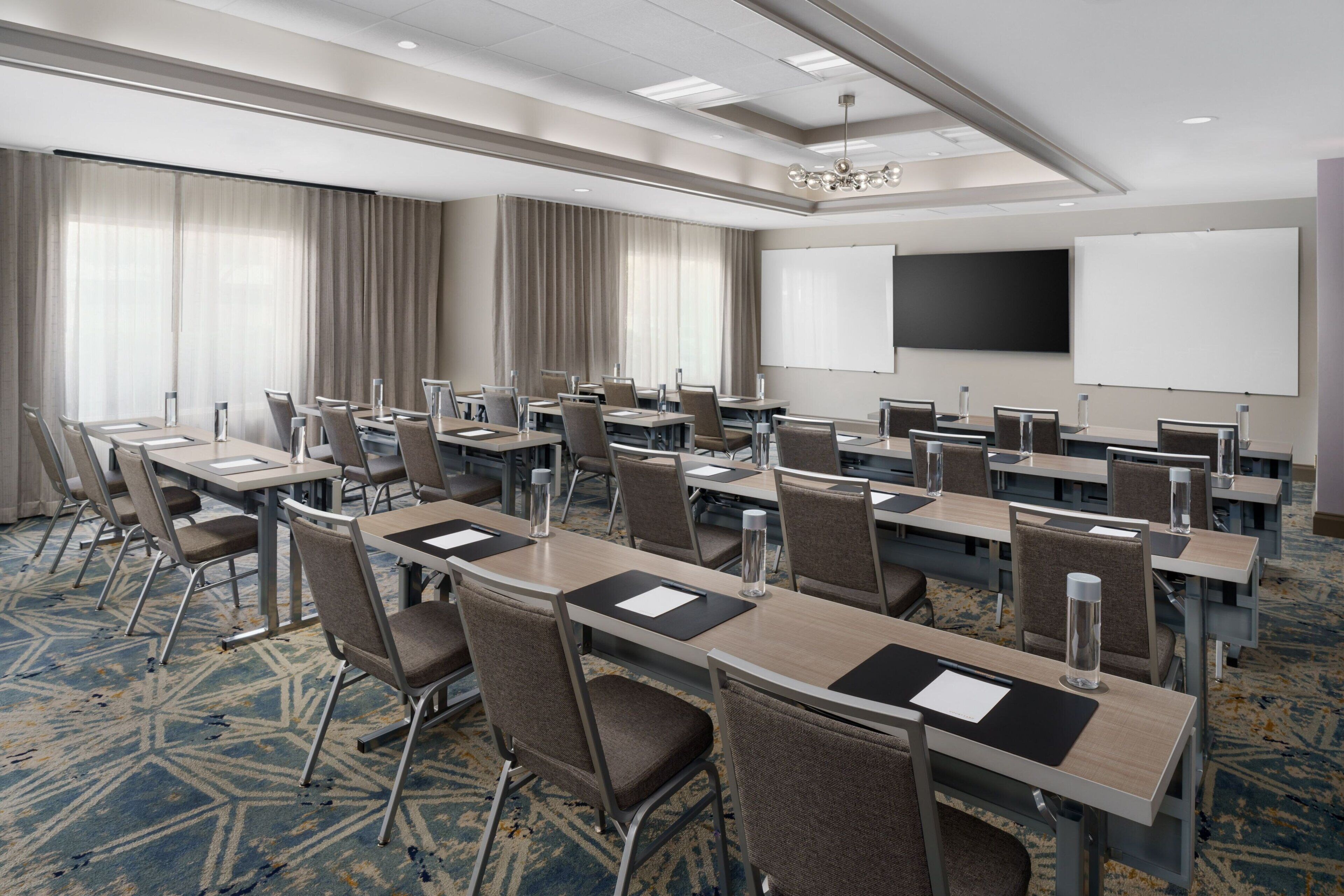 Une salle de conférence équipée de plusieurs tables et chaises, d’un grand tableau blanc et d’un écran de projection.