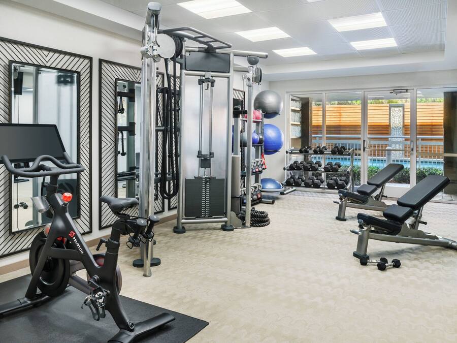 Een sportschool met trainingsapparatuur, spiegels en uitzicht op een zwembad.