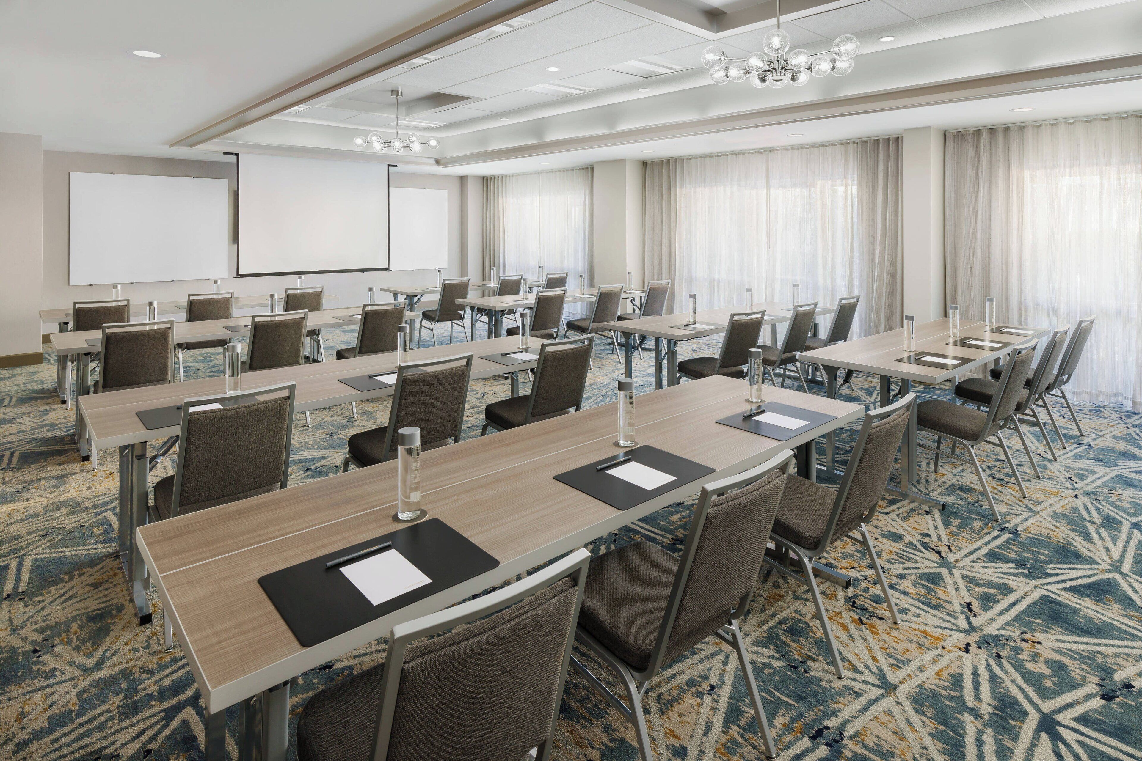 A conference room with multiple tables and chairs, a projector screen, and a large window with curtains.