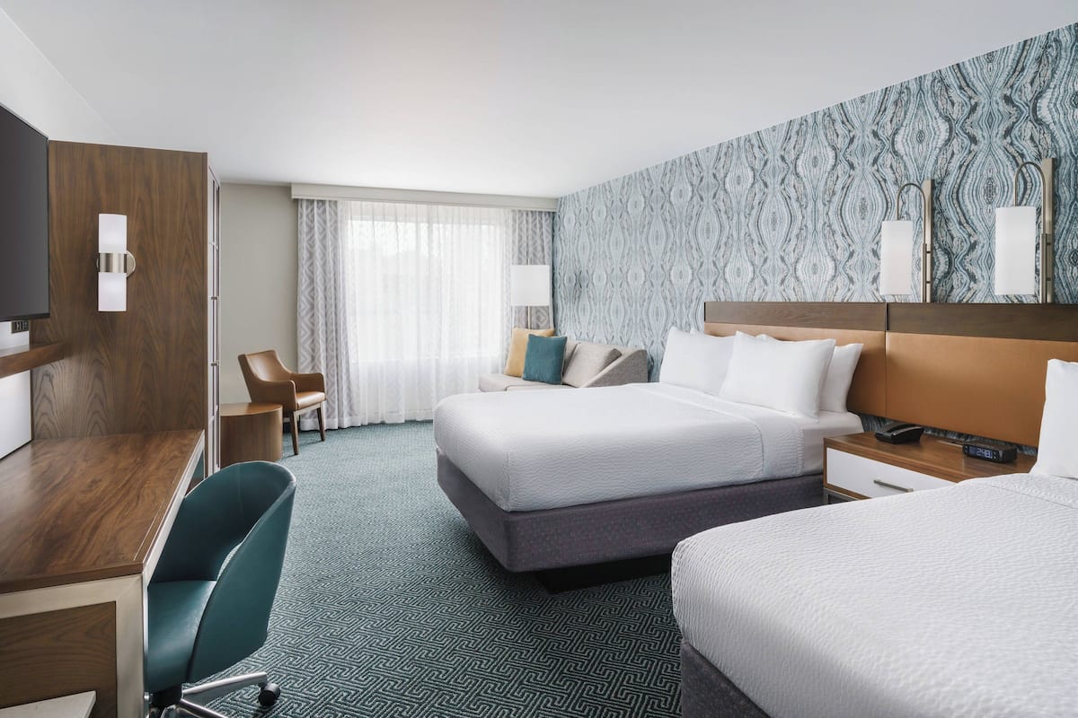 Ein Hotelzimmer mit Bett, Schreibtisch, Sessel, Fernseher und einer Wand mit Muster.