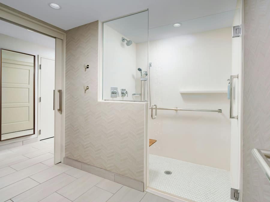 Un baño moderno con ducha de vidrio, piso de azulejos blancos y una puerta con espejo.