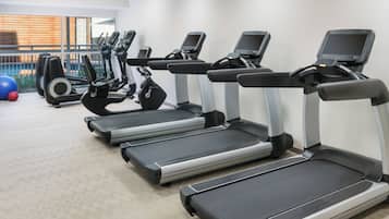 A row of treadmills in a gym with a patterned carpet and a view of a pool through large windows.
