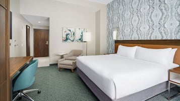 A hotel room with a bed, a desk, a chair, a lamp, and a patterned wall.