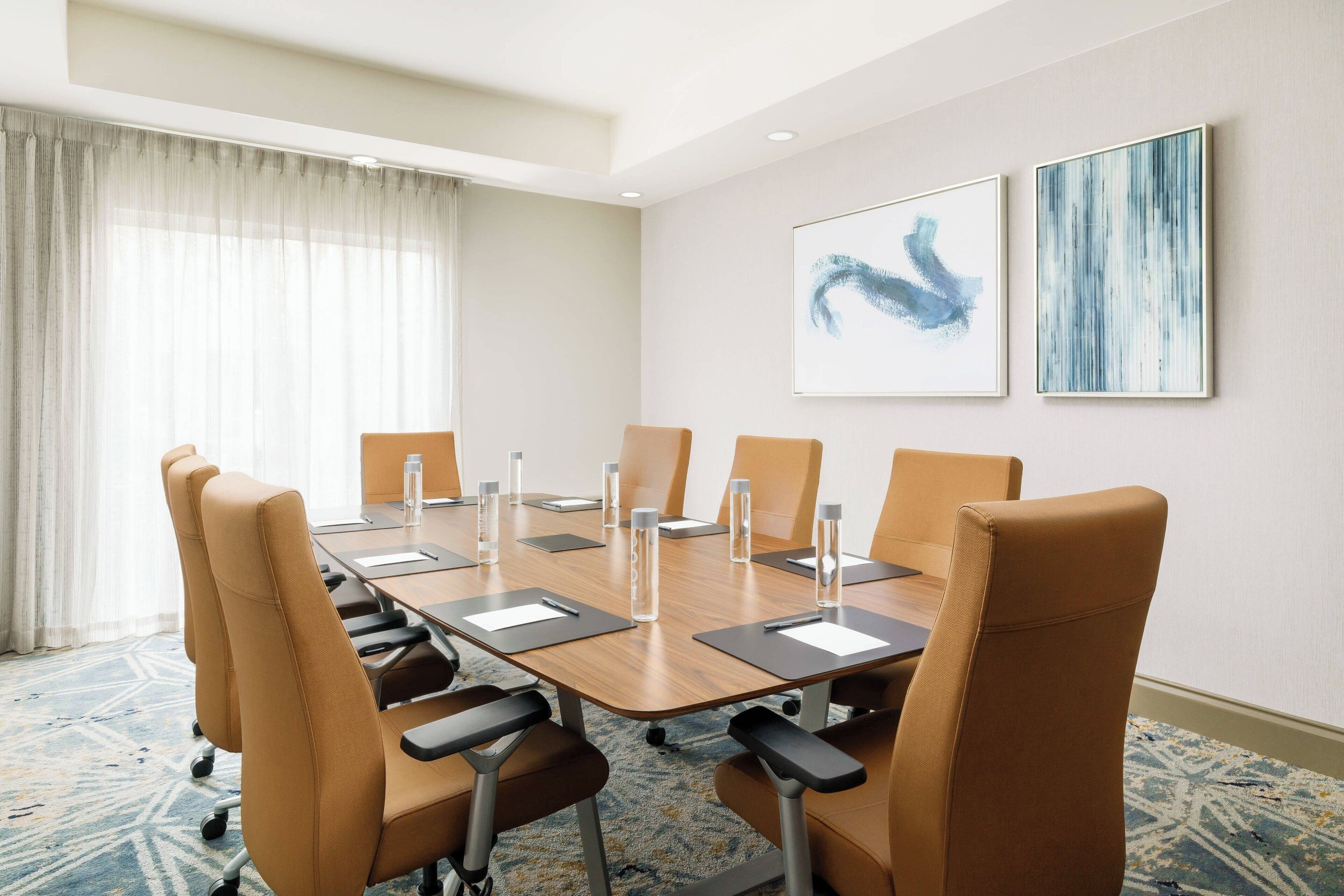 A conference room with a long table, six chairs, and two abstract paintings on the wall.