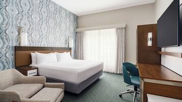 Una habitación de hotel con una cama, un escritorio, una silla, un televisor y una ventana con cortinas.