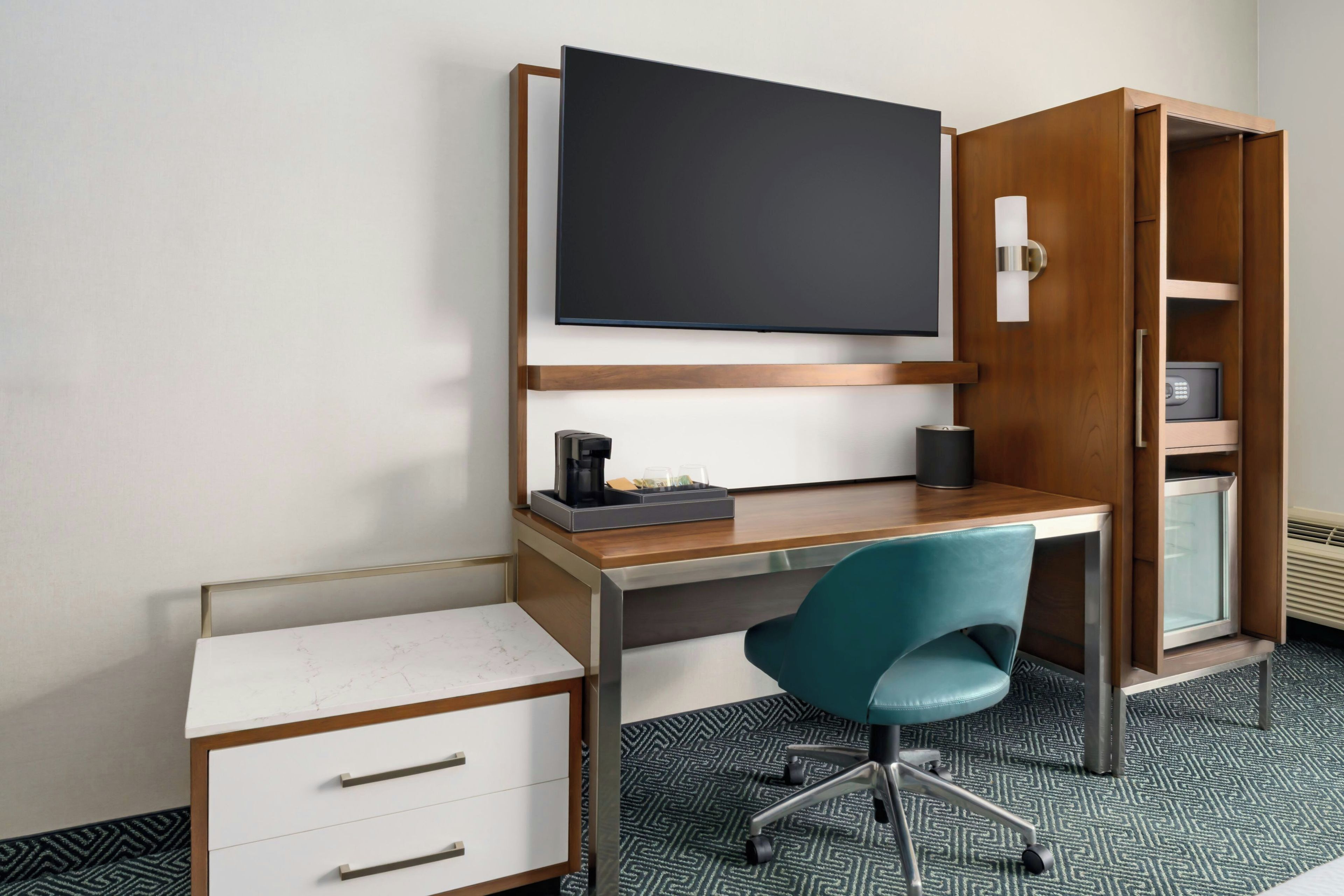 Una habitación de hotel moderna con escritorio, silla y armario con caja fuerte integrada.