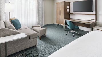 A hotel room with a bed, a sofa, a desk, a chair, and a TV.
