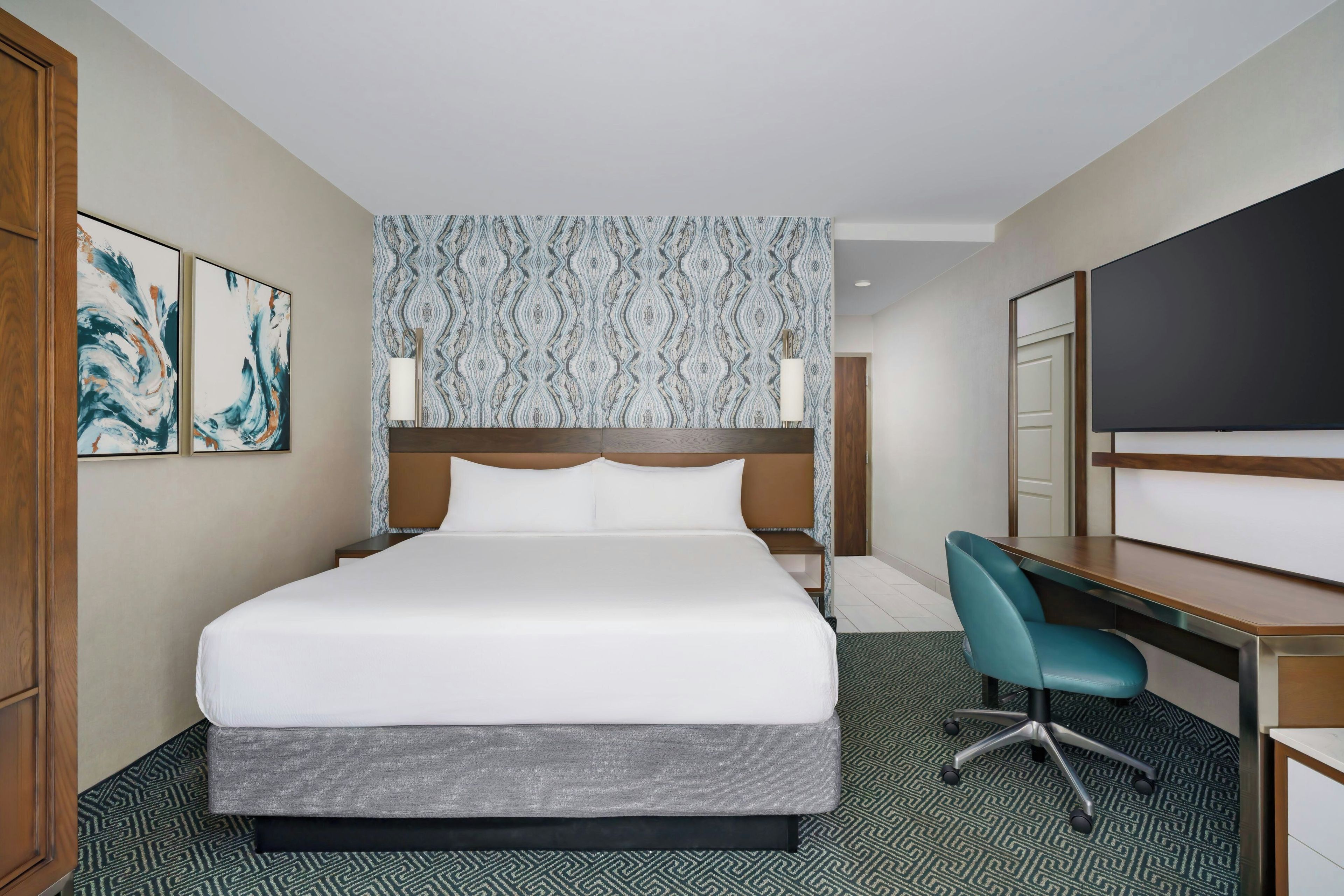 A hotel room with a large bed, a desk, a chair, and a TV.