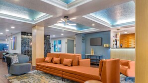 A modern hotel lobby with a sectional sofa, armchairs, a patterned rug, and a reception desk. - Best Western Plus Universal Inn (Orlando)