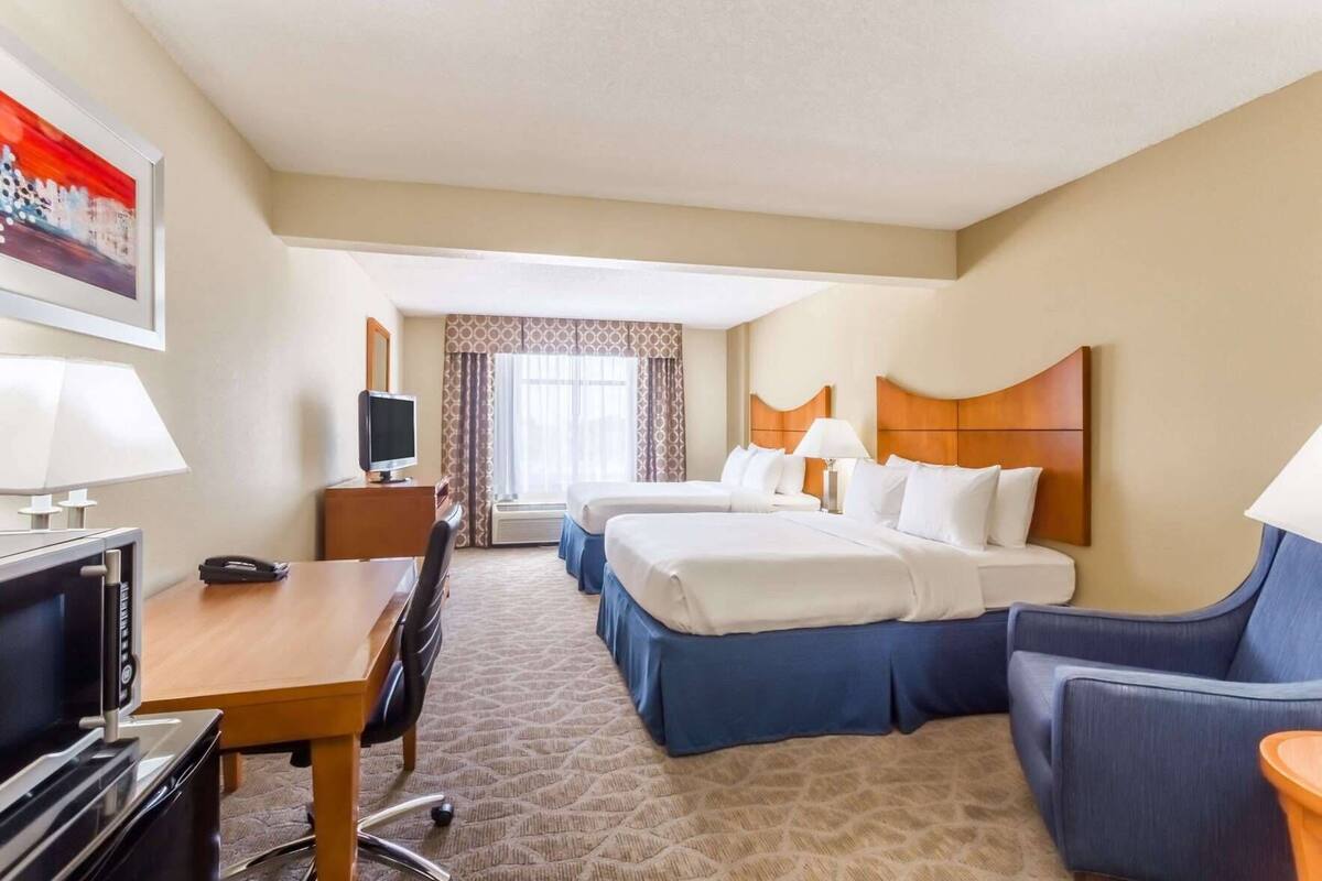 A hotel room with two beds, a desk, a TV, and a chair.