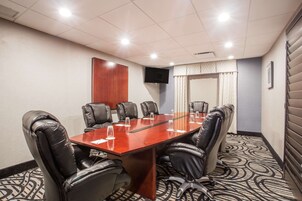A conference room with a long table, leather chairs, a flat-screen TV, and a patterned carpet.