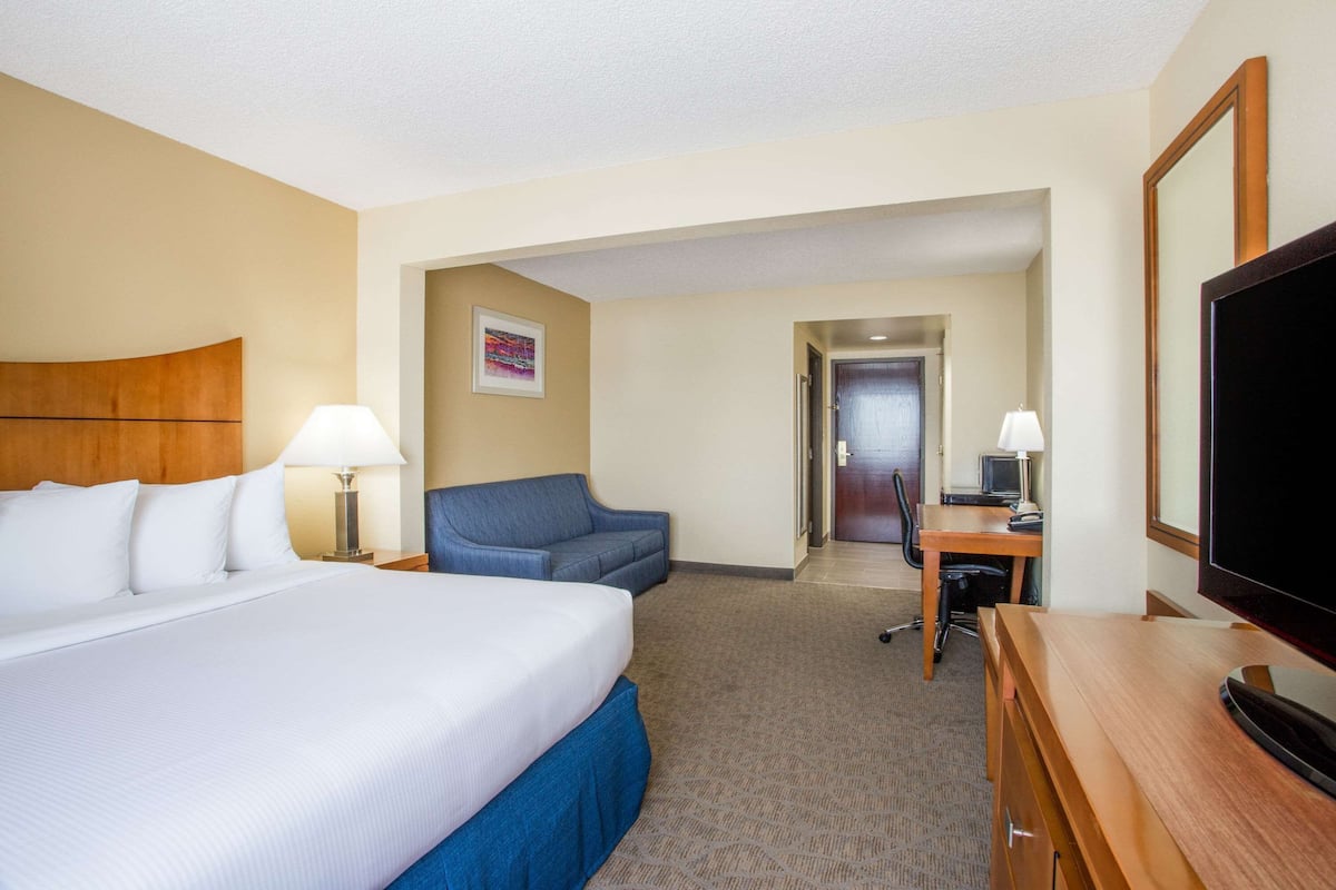A hotel room with a large bed, a desk, a chair, a television, and a door leading to another room.