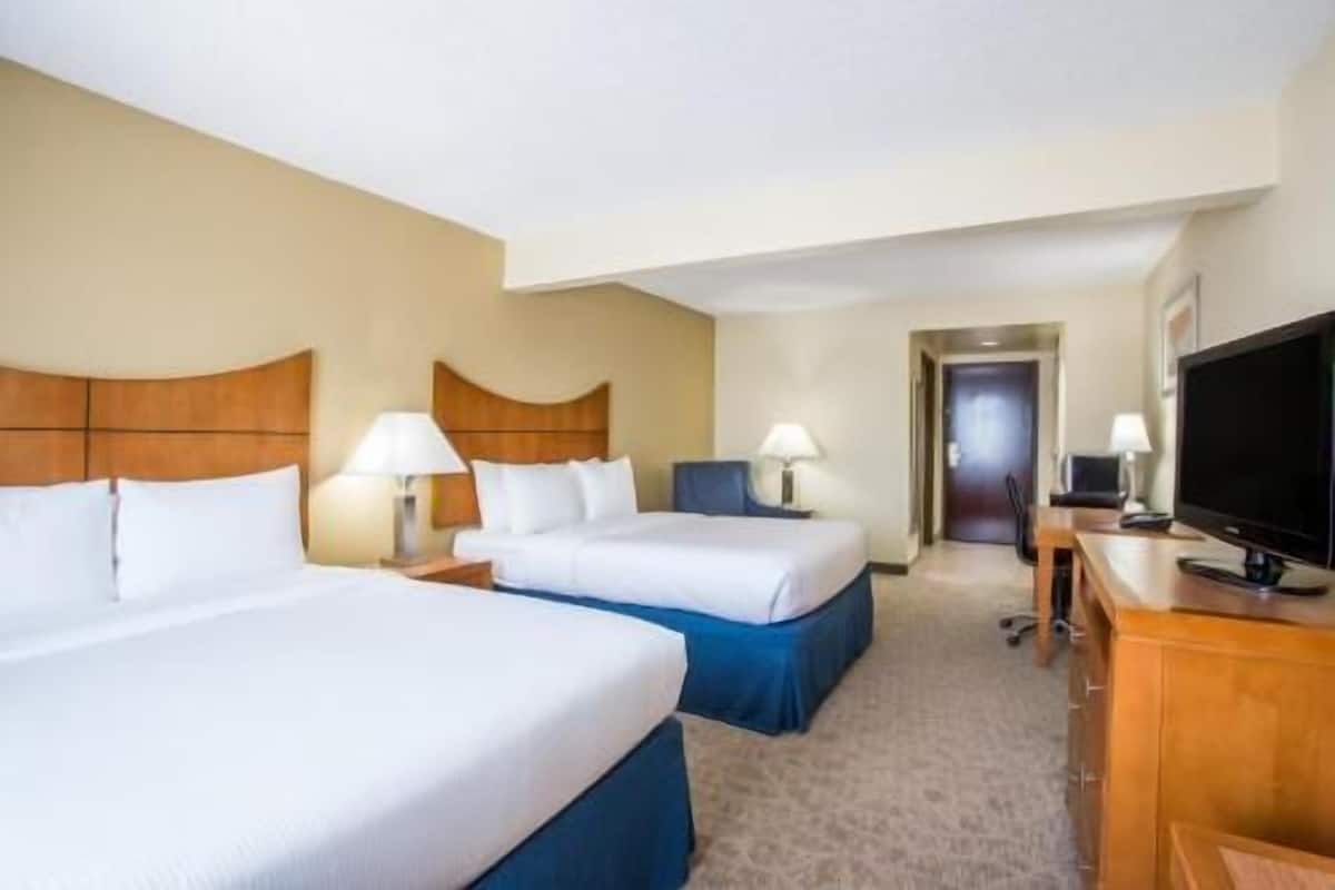A hotel room with two beds, a television, and a desk with a lamp.