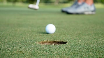 A golf ball on a green with a hole, and a golf club in the background.