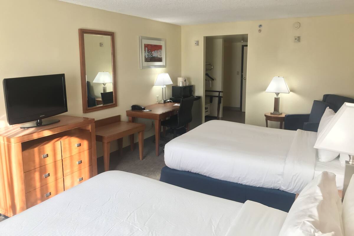 A hotel room with two beds, a desk with a computer, a TV, and two lamps.