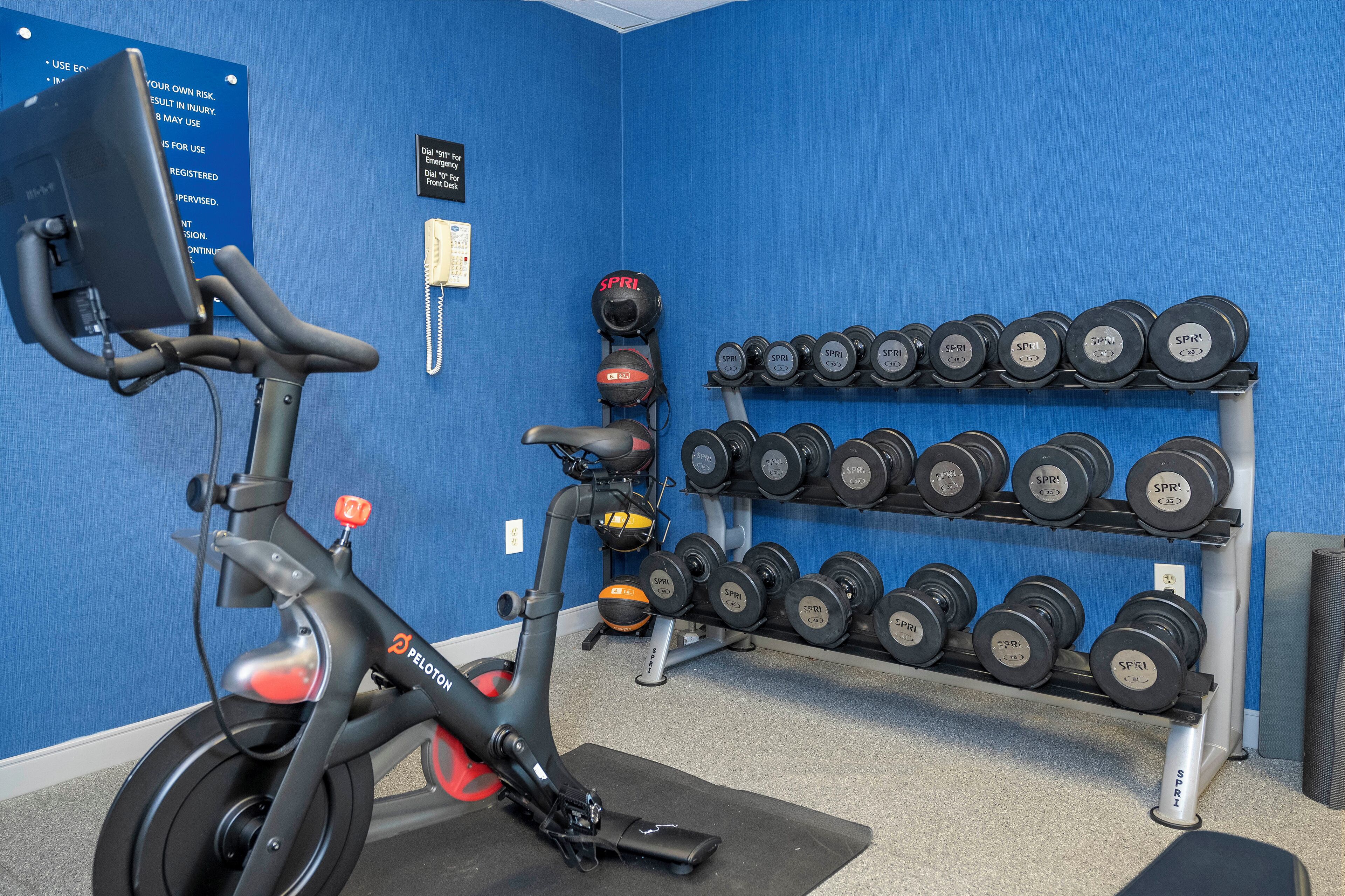 A stationary bike, a wall-mounted phone, and a rack of dumbbells in a room with blue walls.