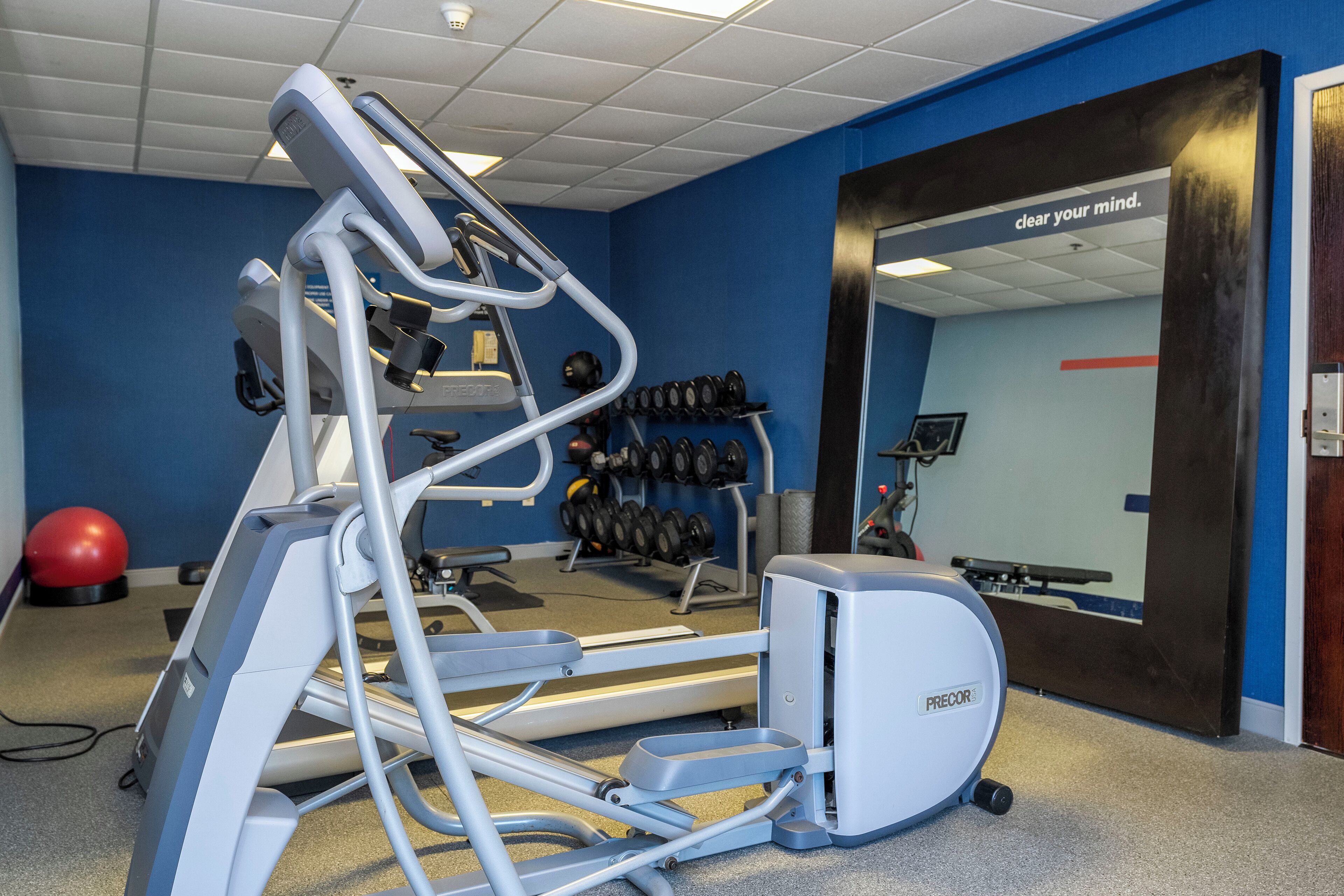 Un gimnasio con equipo de ejercicio, un espejo y una cita motivacional en la pared.