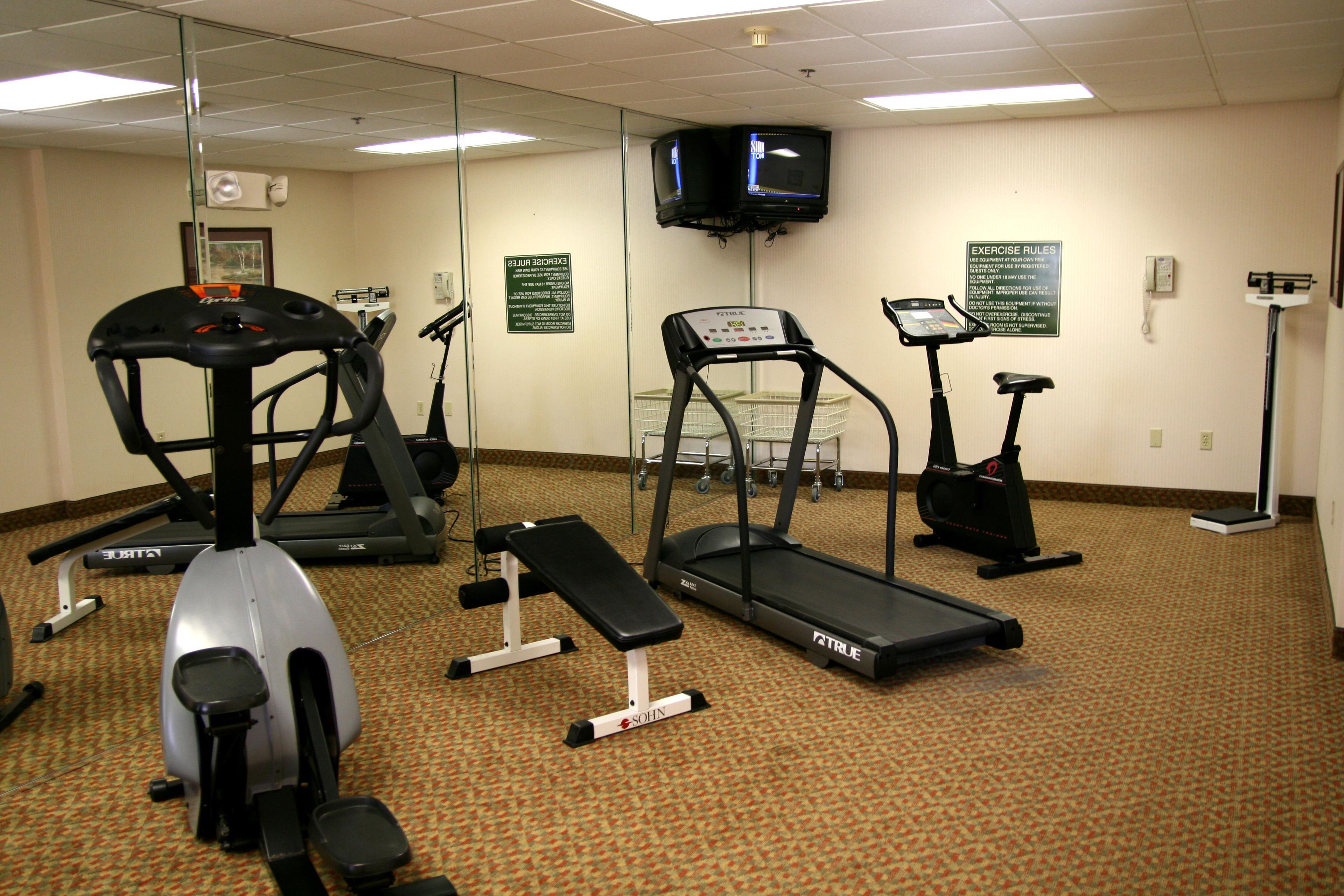 Sala de ginástica com esteiras, elíptico e bicicleta ergométrica.