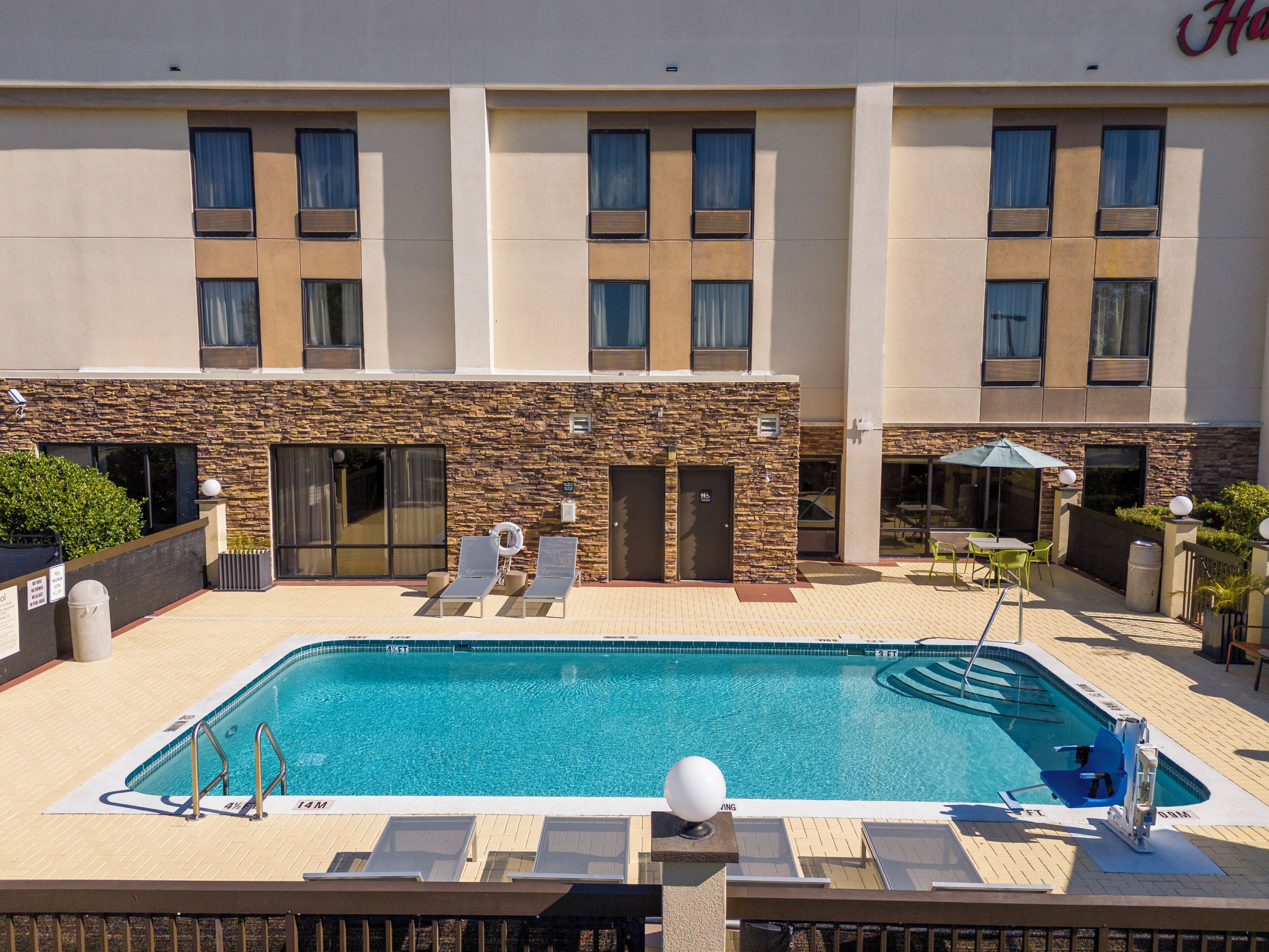 A hotel with a swimming pool, outdoor seating, and a stone facade.