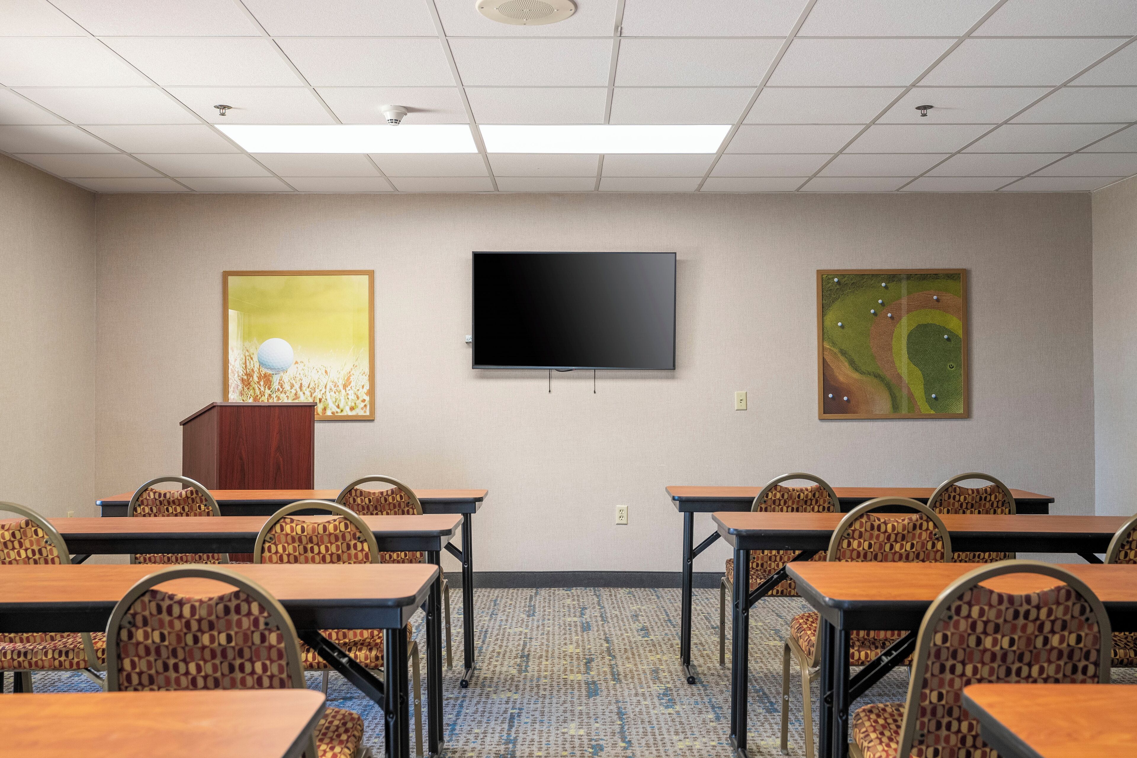 Un salón de conferencias con una televisión de pantalla plana, dos obras de arte enmarcadas y un atril.