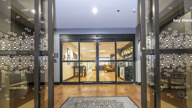 Entrada de un hotel con puerta de cristal, felpudo y cámara de seguridad.