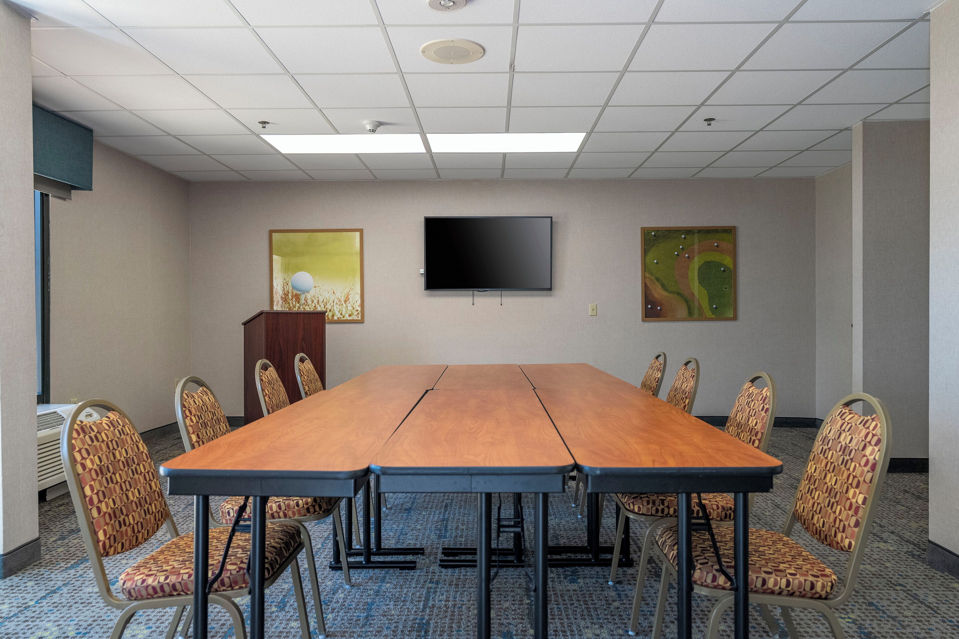 A conference room with a long table, patterned chairs, a flat-screen TV, and two artworks on the walls.