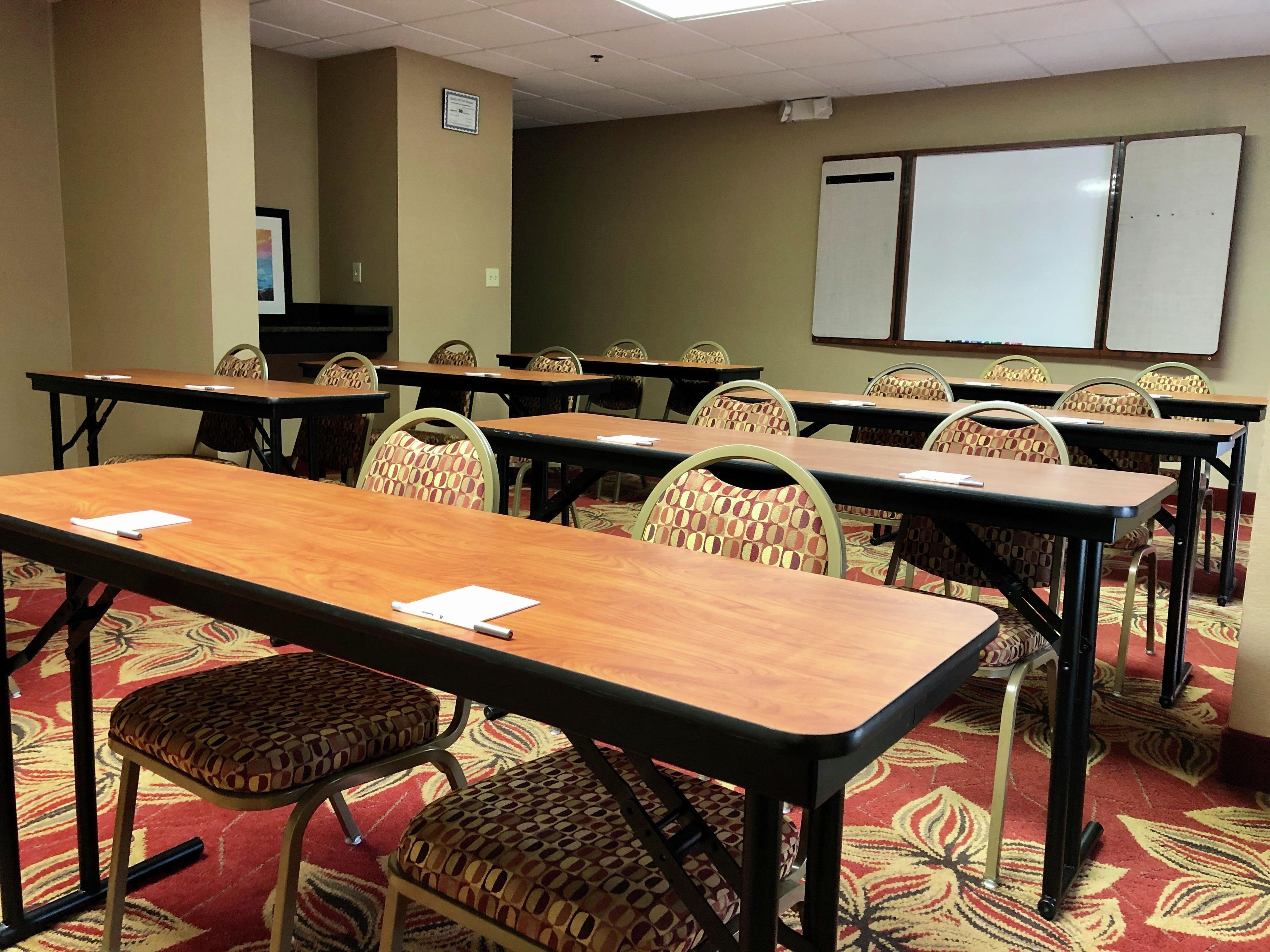 A conference room with multiple tables and chairs, a whiteboard, and a carpeted floor.