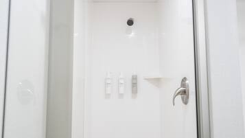 A white shower with a glass door, a showerhead, and three bottles of shampoo on the wall.